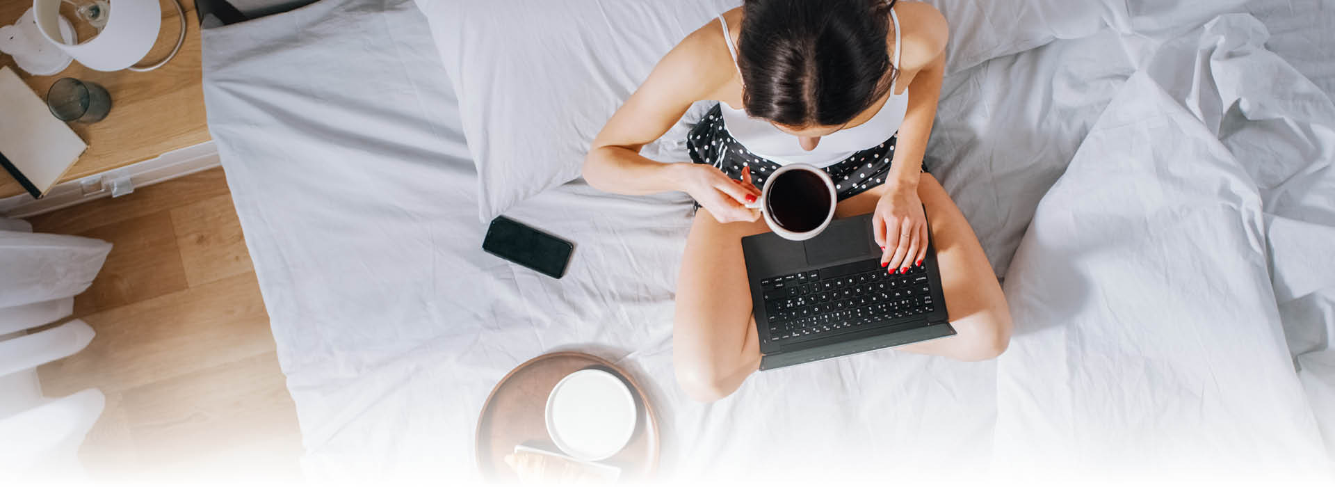 Frau mit Laptop und Kaffee im Bett